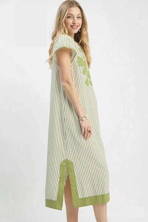 Woman wearing a green and white striped dress with floral details on a white background