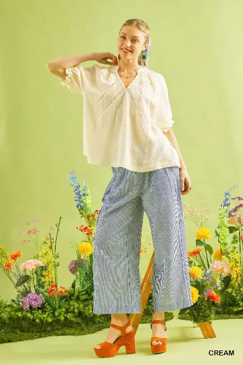 Woman in a white blouse and blue pants standing in front of colorful flowers with a green background.