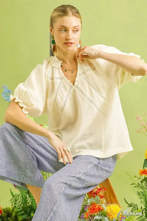 Woman in a white blouse and striped pants sitting on a wooden stool with a green background