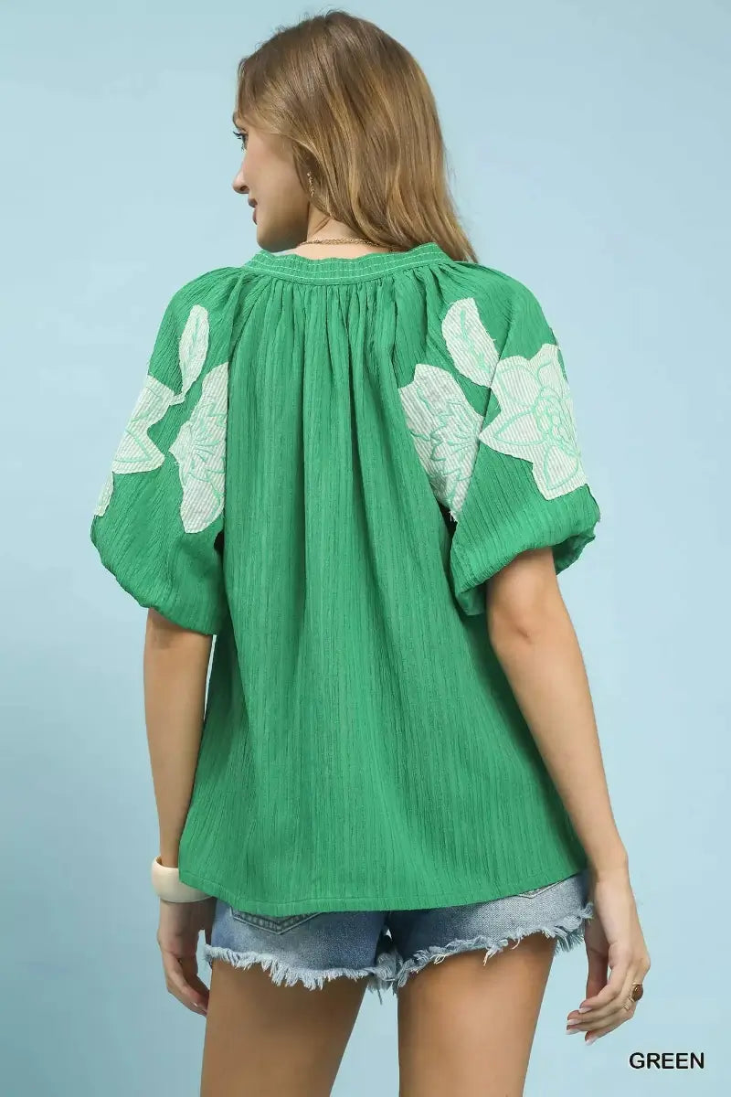 Woman wearing a green blouse with floral patterns on a light blue background