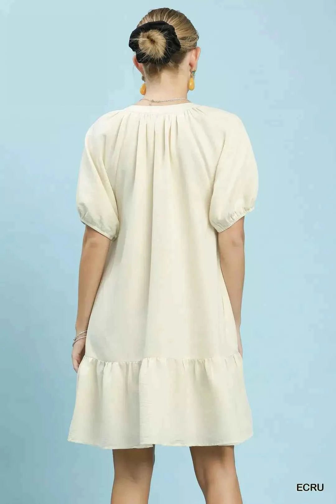 Woman wearing a cream-colored dress against a light blue background facing away from camera