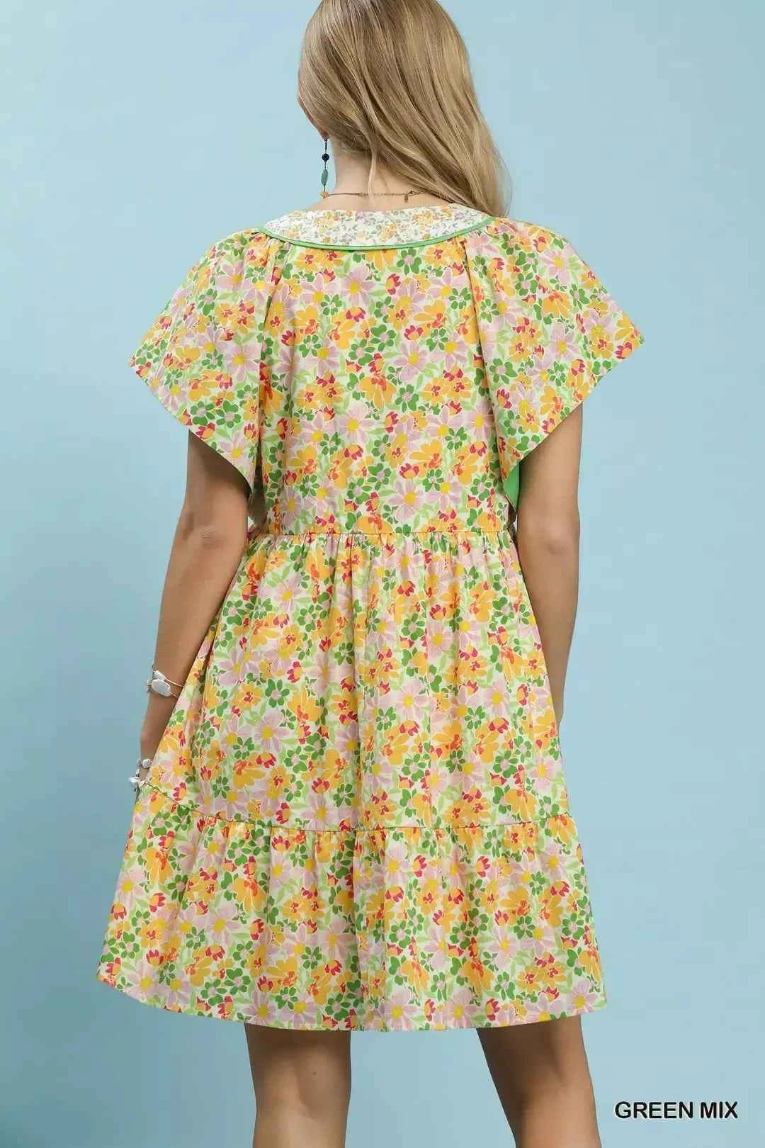 Woman wearing a floral dress against a light blue background facing wall