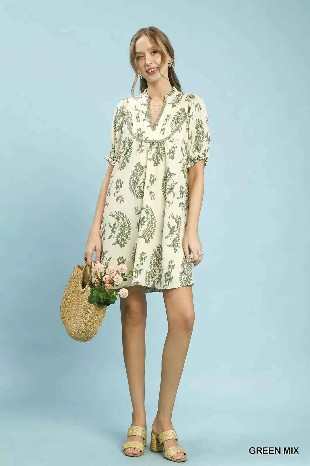 Woman wearing a floral dress holding a straw bag against a light blue background