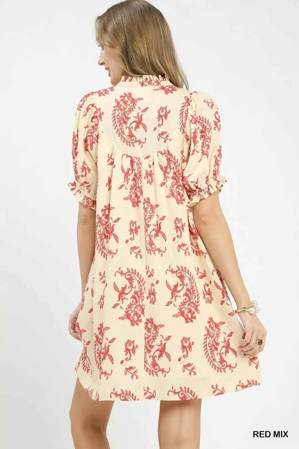 Woman wearing a cream dress with red floral pattern on a white background