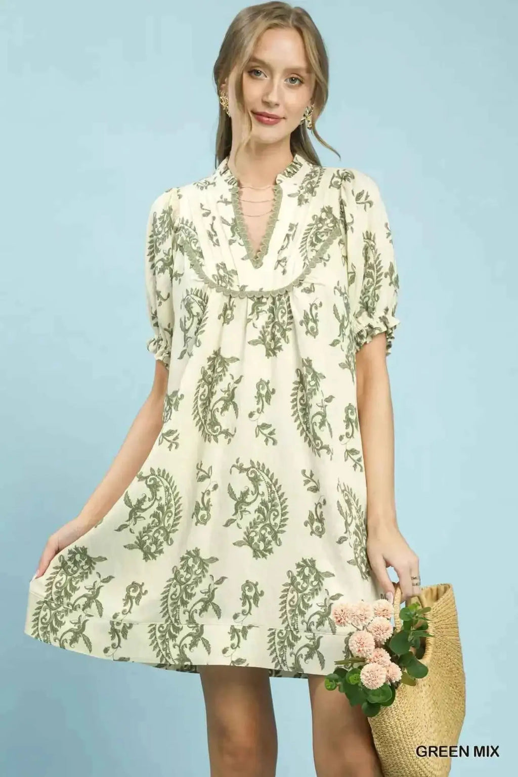 Woman wearing a floral dress holding flowers against a light blue background