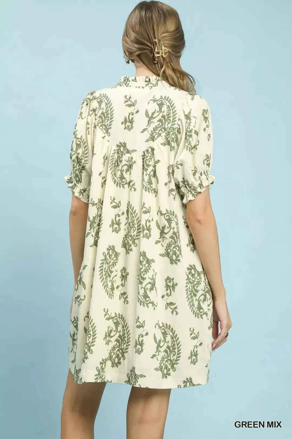 Woman wearing a floral dress against a light blue background facing wall