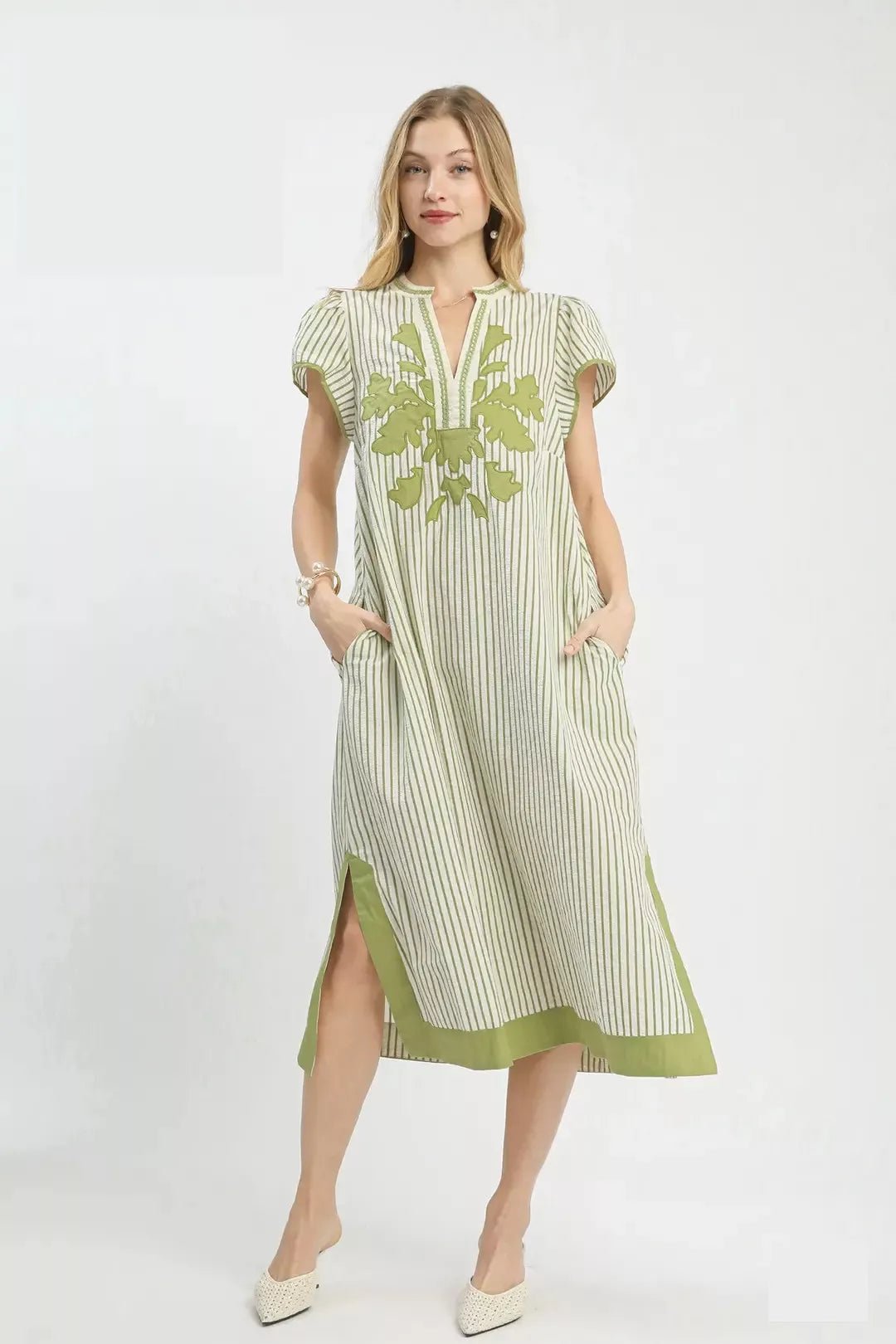 Woman wearing a green and white striped dress with floral embroidery on a white background