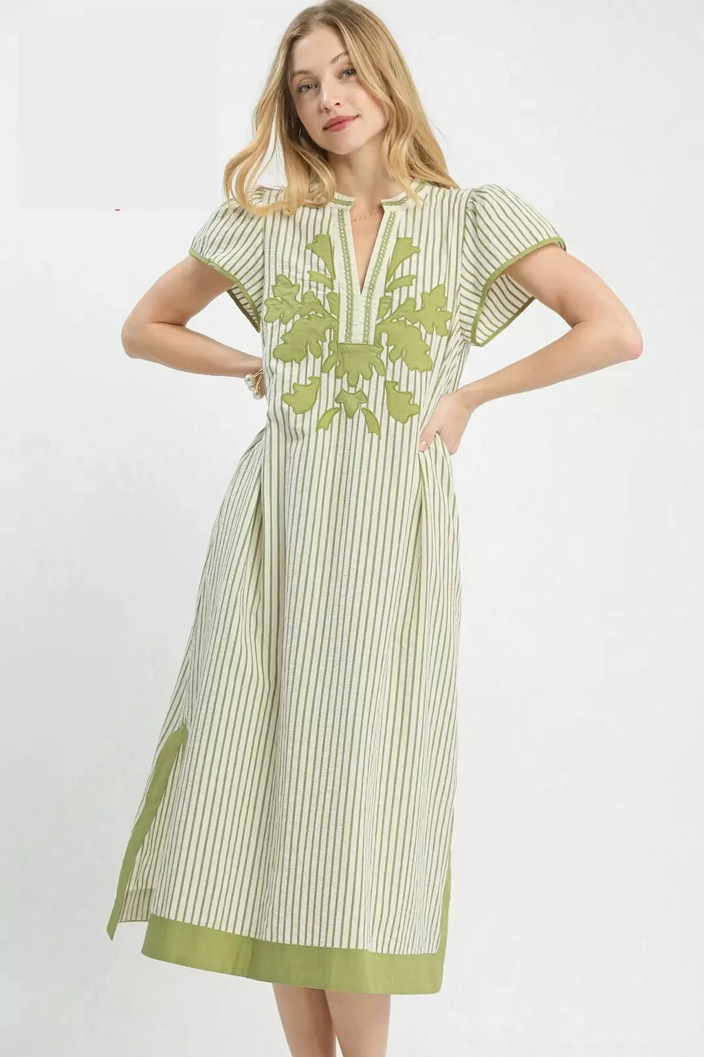 Woman with hands on waist wearing a green and white striped dress with floral embroidery on a white background