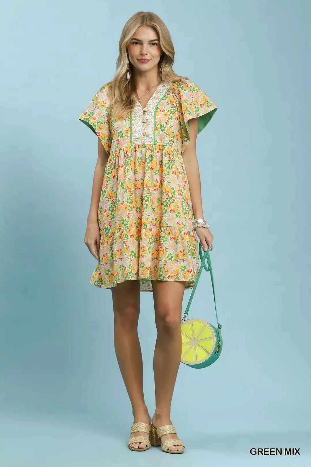 Woman wearing a floral dress holding a green handbag against a light blue background