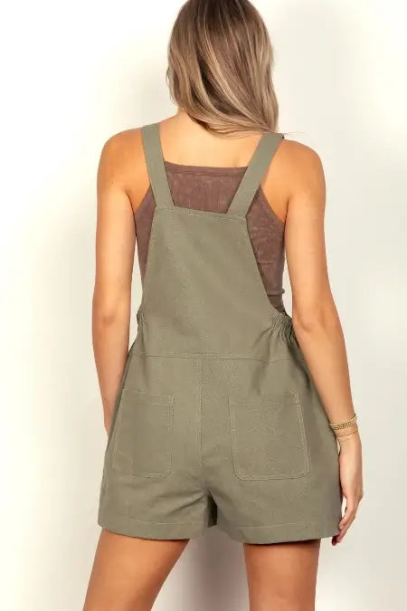 Person wearing a green overall romper on a plain background