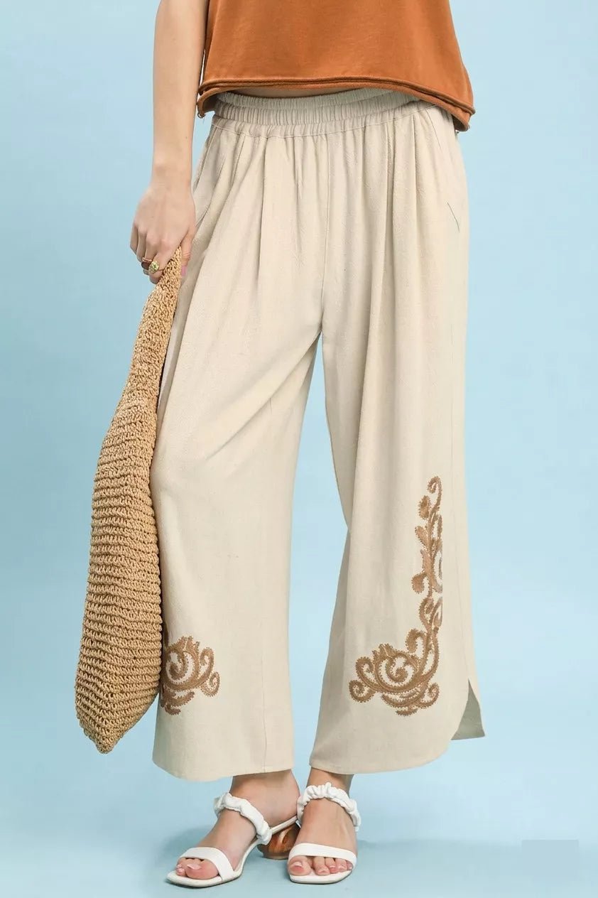 Beige pants with gold embroidery worn by a person on a light blue background