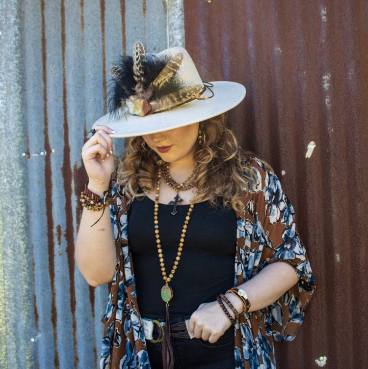 Woman wearing a feathered hat and patterned kimono against a rusty metal wall.