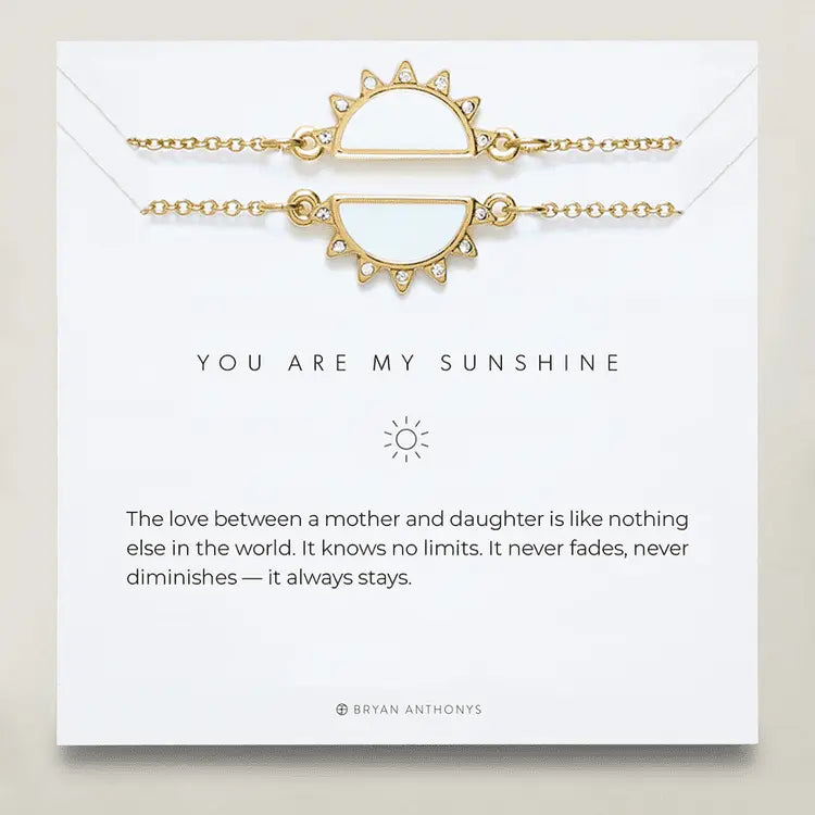 Matching pair of gold half-sun bracelets with white centers on branded card