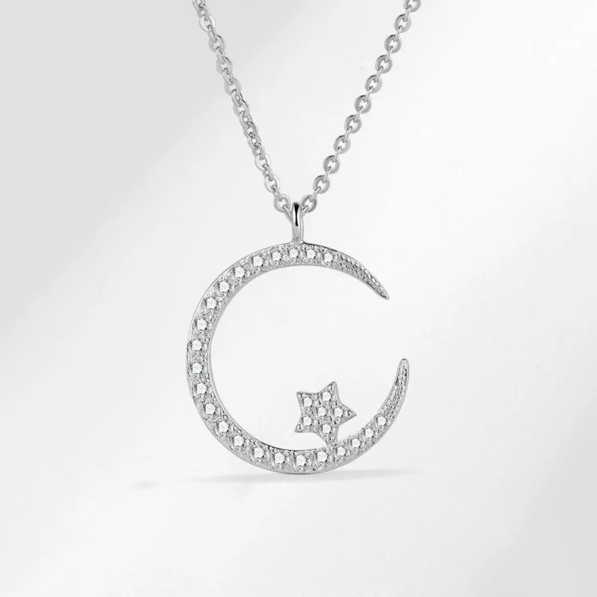 Silver necklace with a crescent moon and star pendant on a light gray background