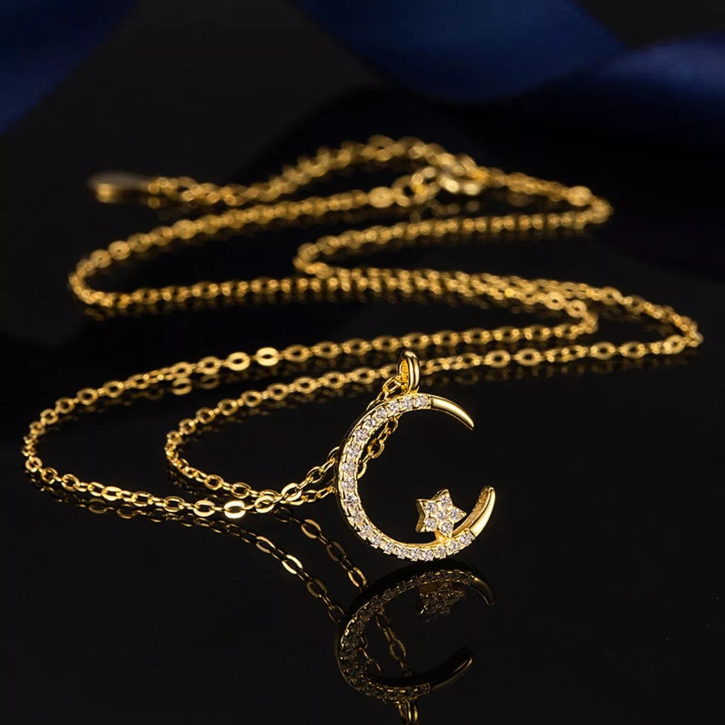 Gold necklace with a crescent moon and star pendant on a reflective surface.