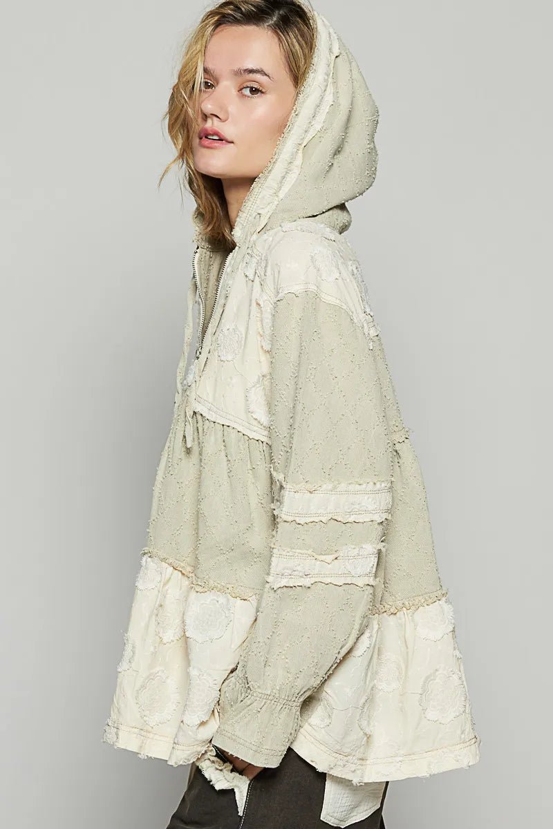 Woman wearing a light-colored hooded jacket with lace details on a plain background